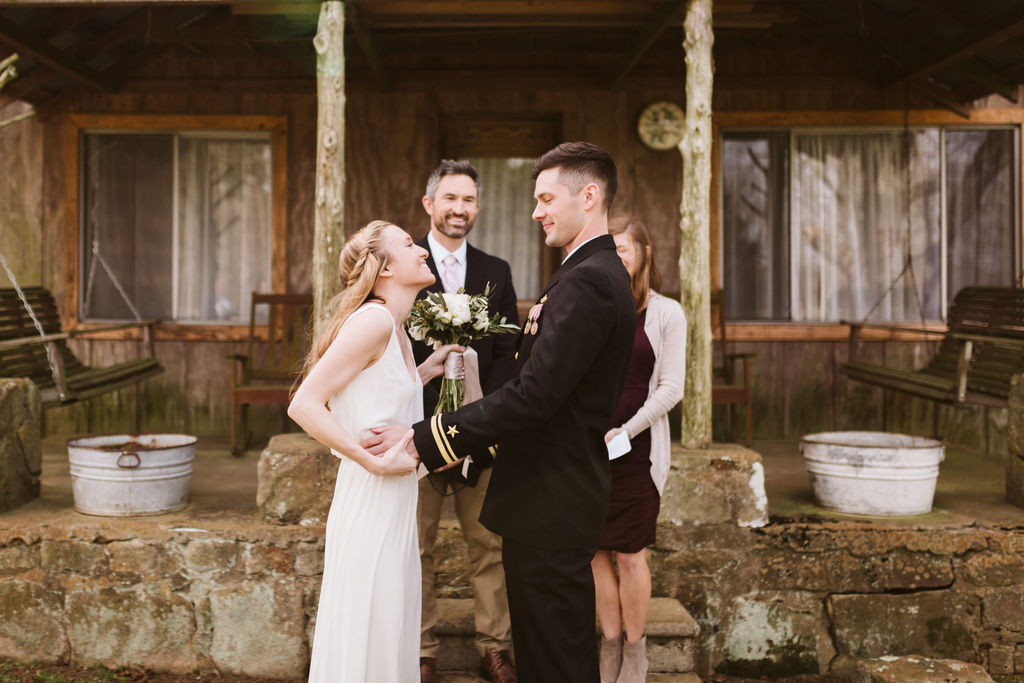 Bride and groom facing each other holding hands in front of antique family cabin porch
