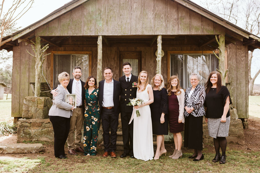 Bride and groom stand with their family members in front of antique family cabin front porch