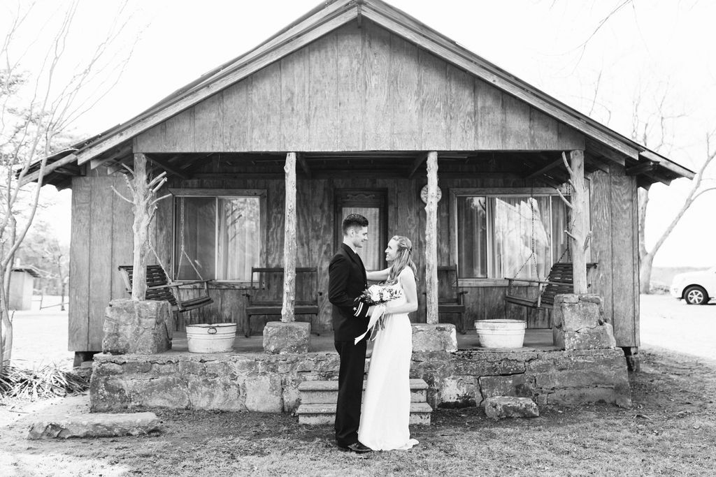 Bride and groom stand facing each other in front of antique family cabin's front porch