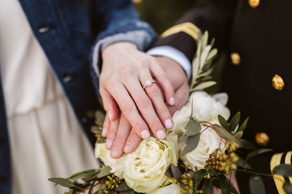 Bride and groom place hands on top of bouquet, her hand on top showing off her wedding ring