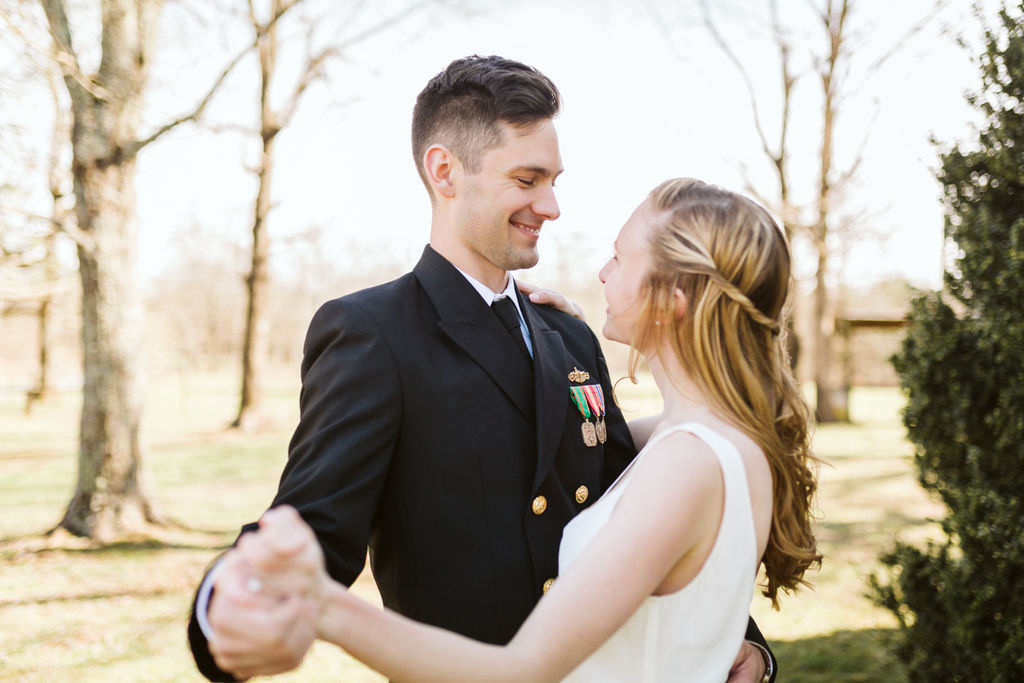 Bride and groom share a dance in front of greenery, they look into each other's faces