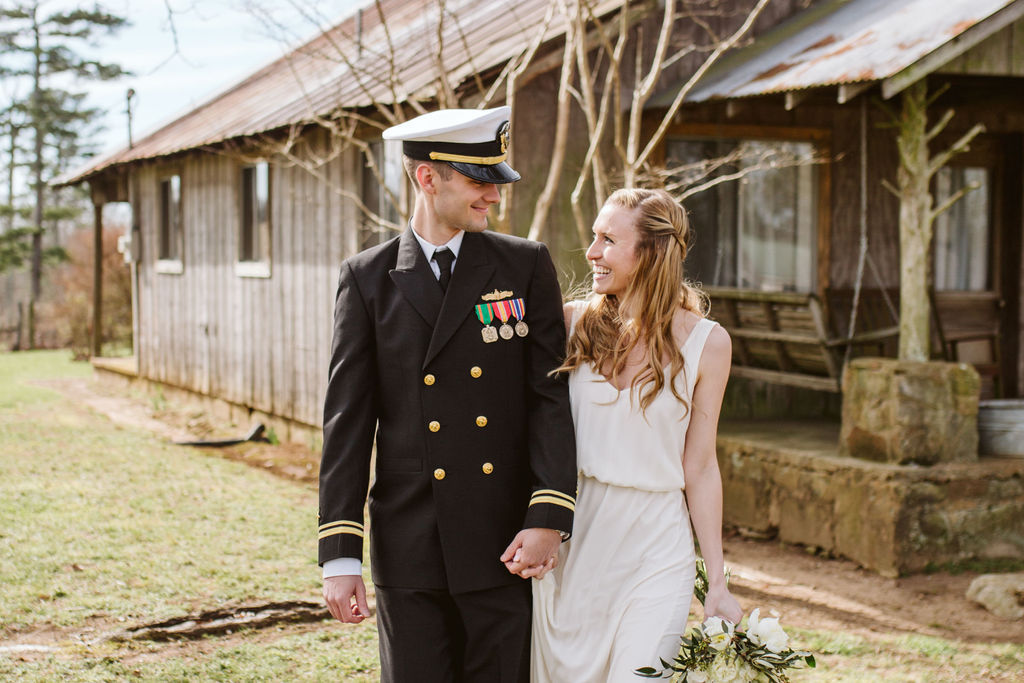 Groom in military dress uniform holds his bride's hand as they smile at each other