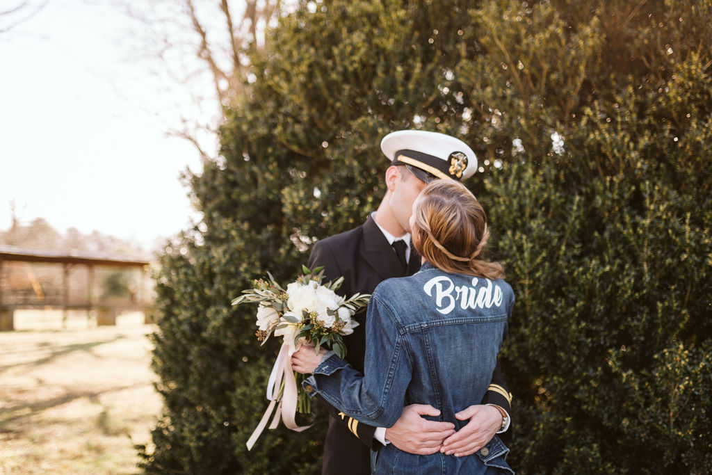 Bride kisses groom while wearing her customized bride denim jacket with the word "Bride" painted across the back