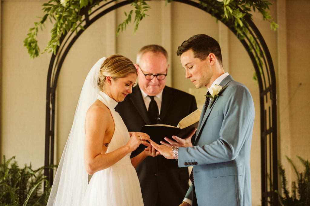 Bride slides ring onto groom's finger under simple floral archway during Lookout Mountain wedding ceremony