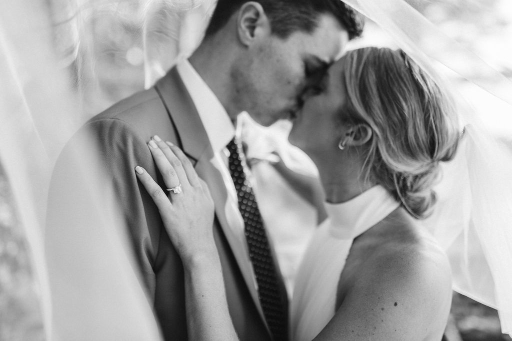 Bride and groom kiss under bride's veil, her left hand on his chest