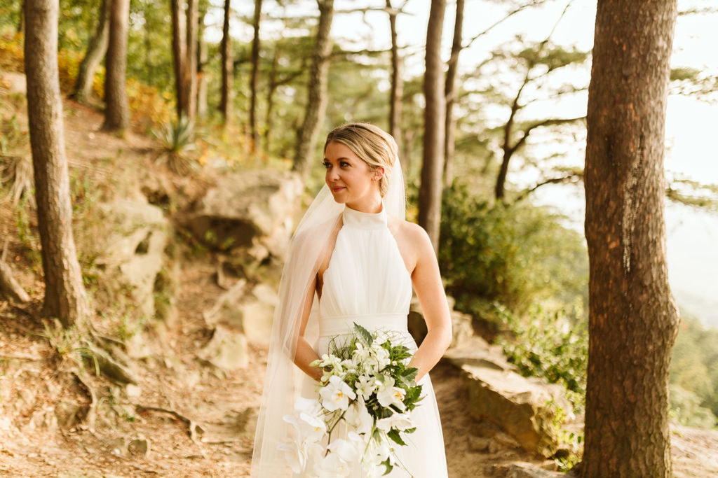 Bride holding bouquet looks over her right shoulder into the woods during portraits at Sunset Rock in Chattanooga, Tennessee
