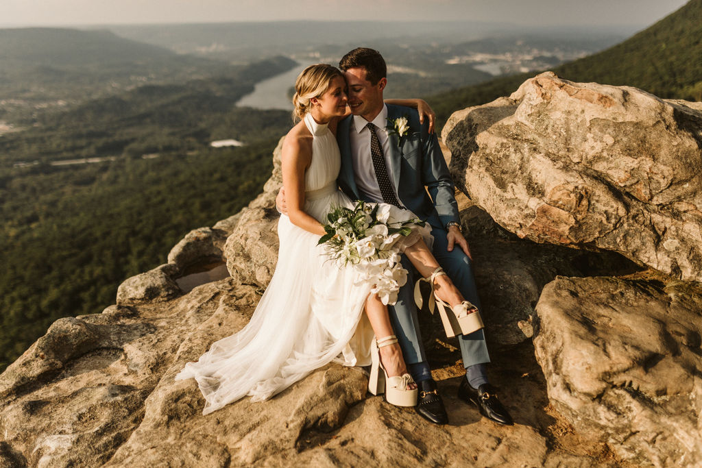 Bride and groom snuggle atop Sunset Rock after their wedding on Lookout Mountain, her legs across his lap.