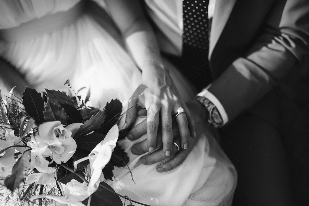 Bride's hand with emerald cut ring over groom's hand with wedding band.