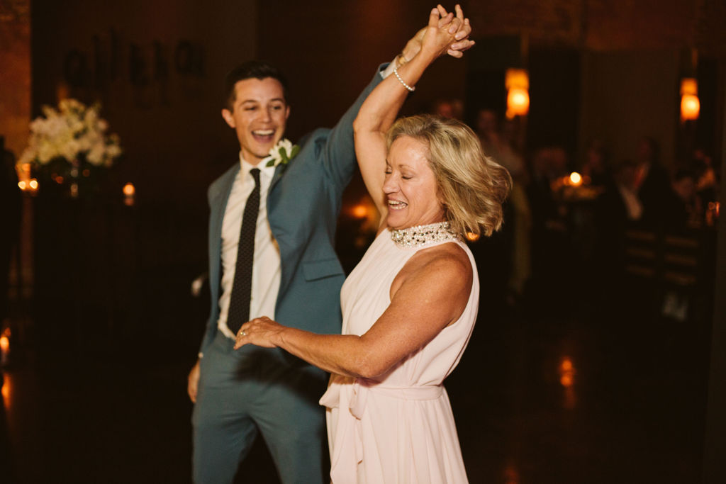 Groom smiles widely as he twirls his mother during their dance at wedding reception