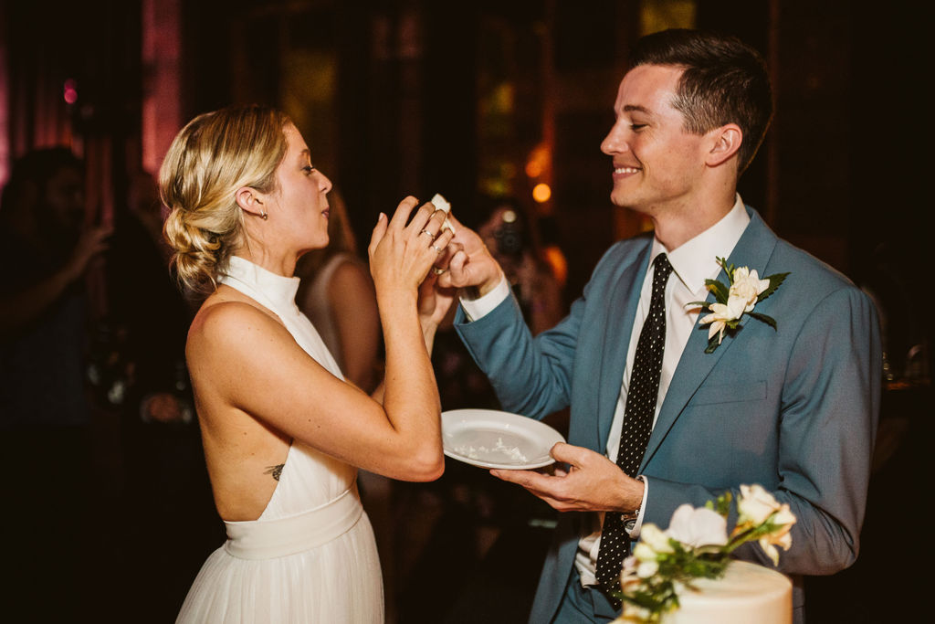 Groom playfully reaches to feed bride a bite of wedding cake