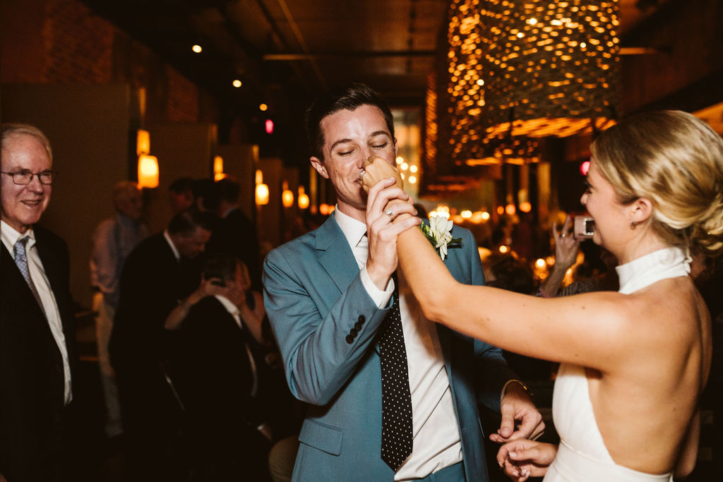Bride playfully reaches to feed groom a bite of wedding cake while he holds her hand