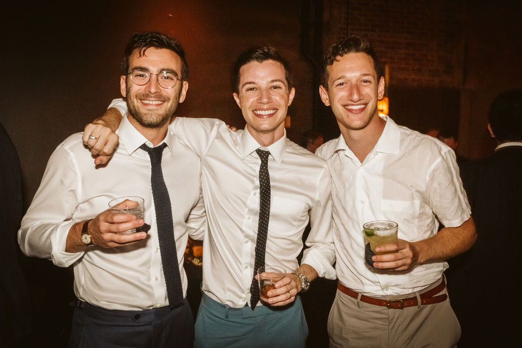 Groom stands in his shirtsleeves with his arms around 2 friends during downtown Chattanooga wedding reception