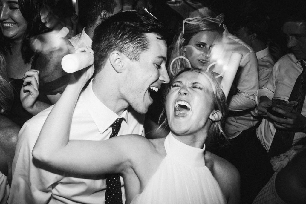 Groom stands behind bride her arm around his neck while they sing to each other