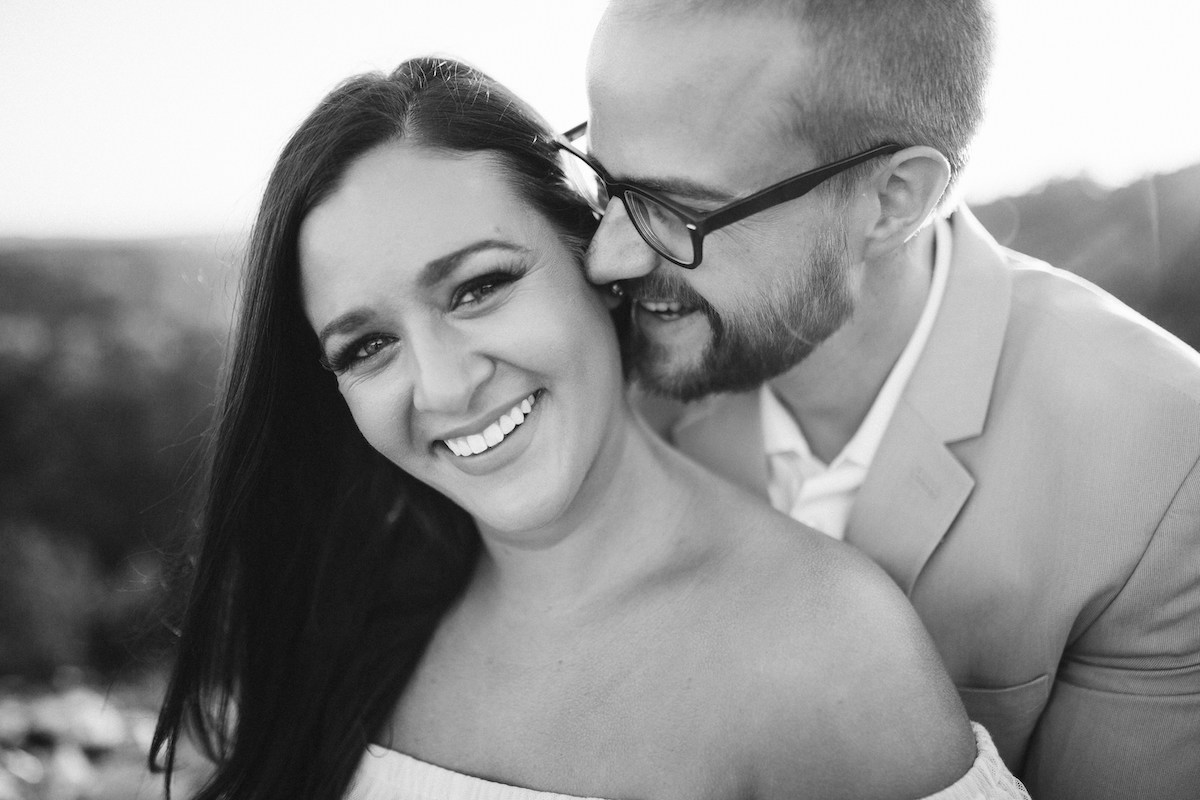 Man leans over woman's shoulder, almost kissing her neck while they both smile