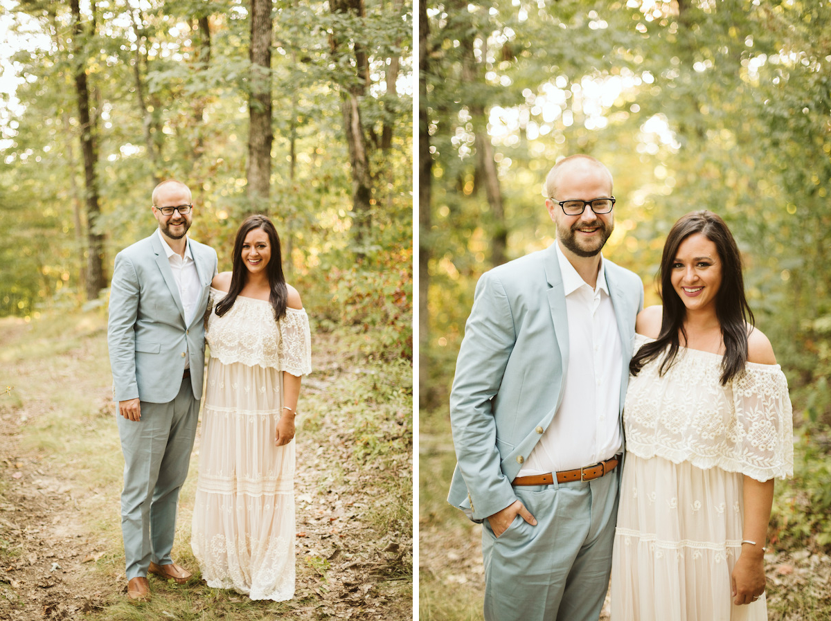 Man in light blue suit and woman in white lacy dress stand beneath tall trees on Raccoon Mountain