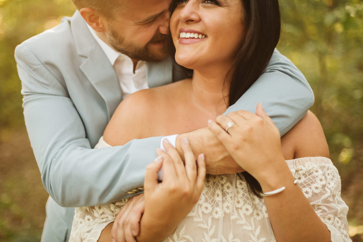 Man leans over woman's shoulder, almost kissing her neck while they both smile