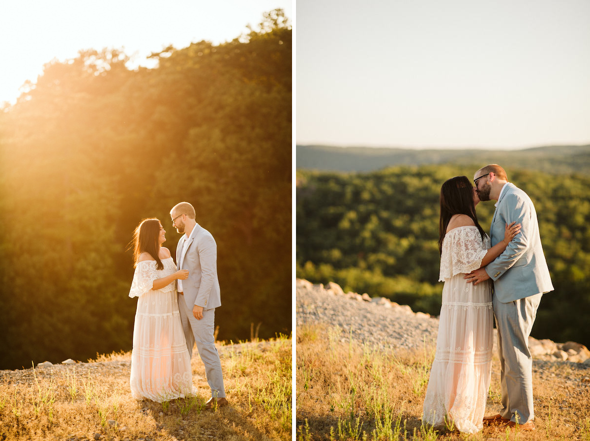Man in light blue suit and woman in flowing lacy white dress kiss at sunset with rolling Tennessee Valley hills behind them