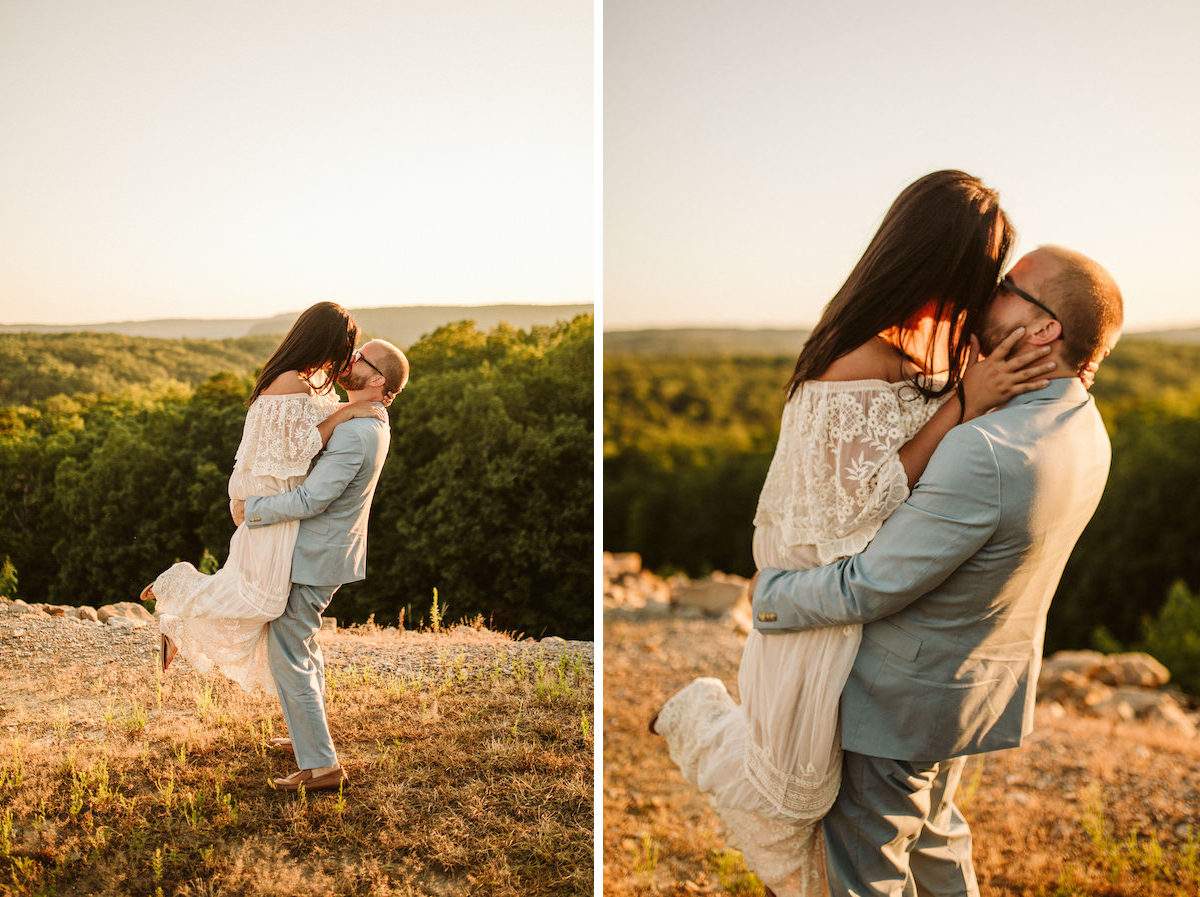 Man in light blue suit picks up woman in flowing lacy white dress with rolling Tennessee Valley hills behind them