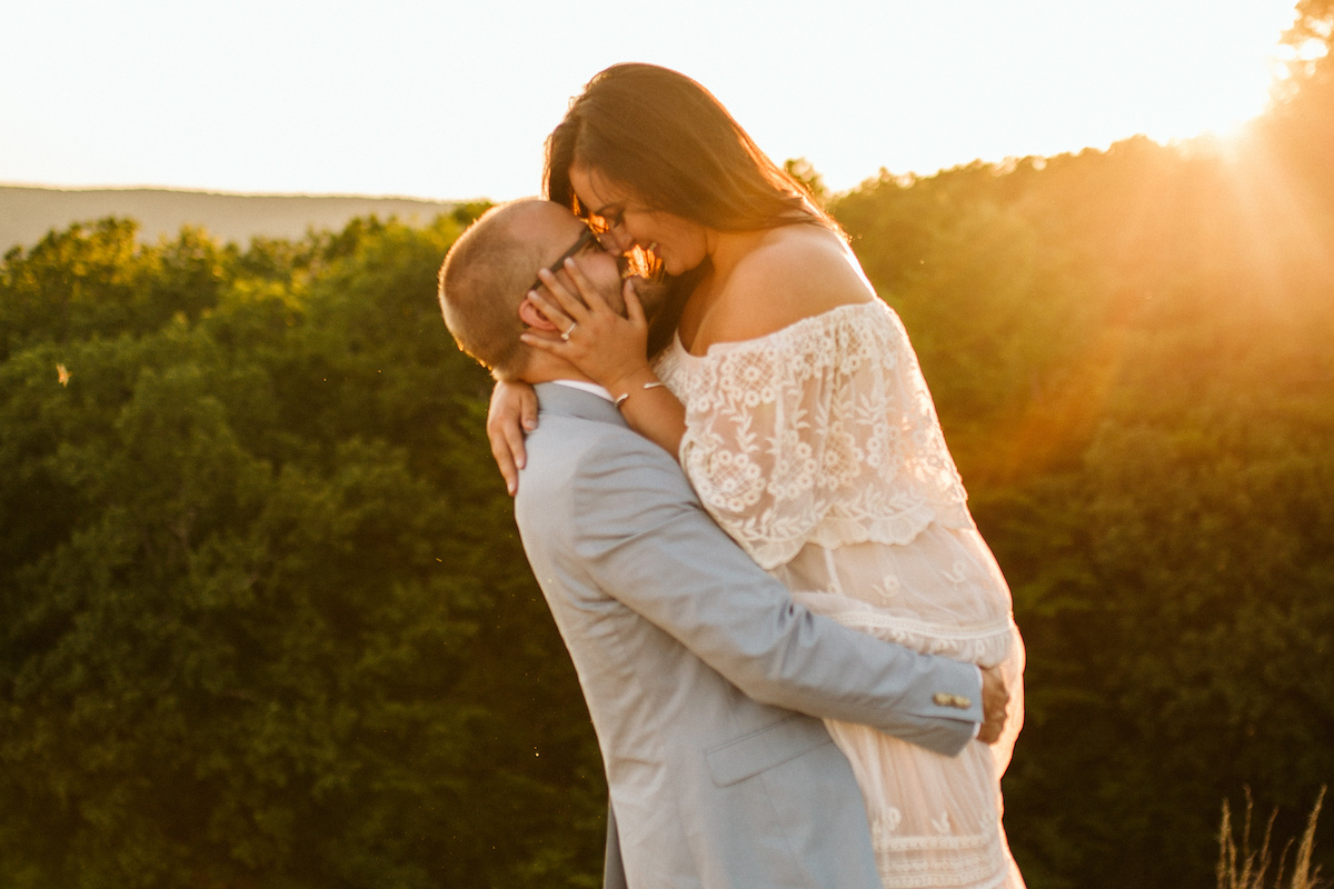 Man in light blue suit picks up woman in flowing lacy white dress with rolling Tennessee Valley hills behind them