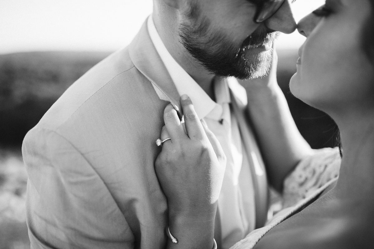 Man in light blue suit and glasses leans nose-to-nose with woman at sunset during Raccoon Mountain engagement session