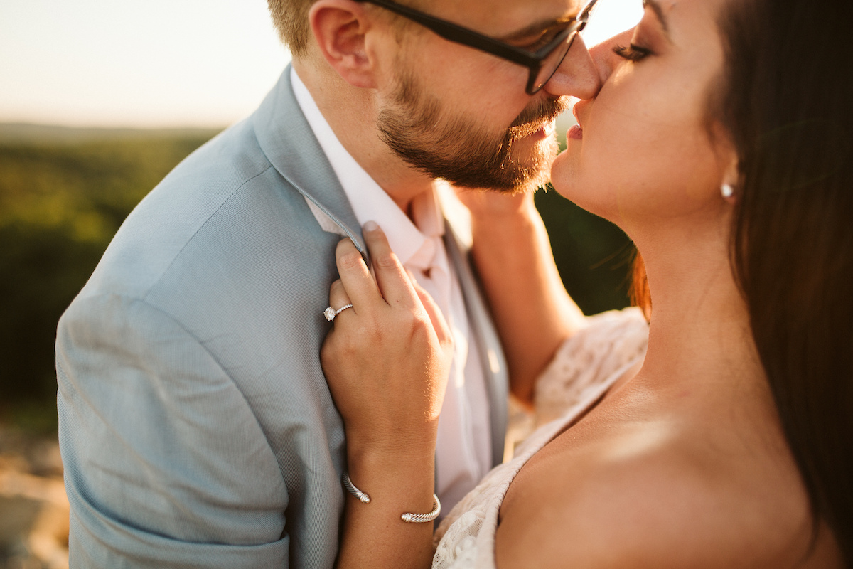 Man in light blue suit and glasses leans in to kiss woman at golden hour during Raccoon Mountain engagement session