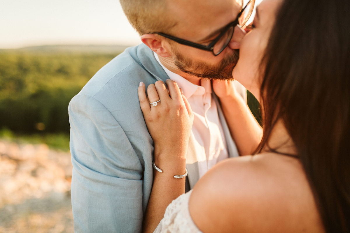 Man in light blue suit and glasses leans in to kiss woman at golden hour during Raccoon Mountain engagement session