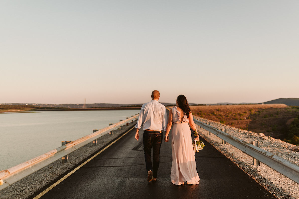Man and woman walk hand-in-hand on Raccoon Mountain's loop drive at golden hour. She carries a bouquet of white flowers.