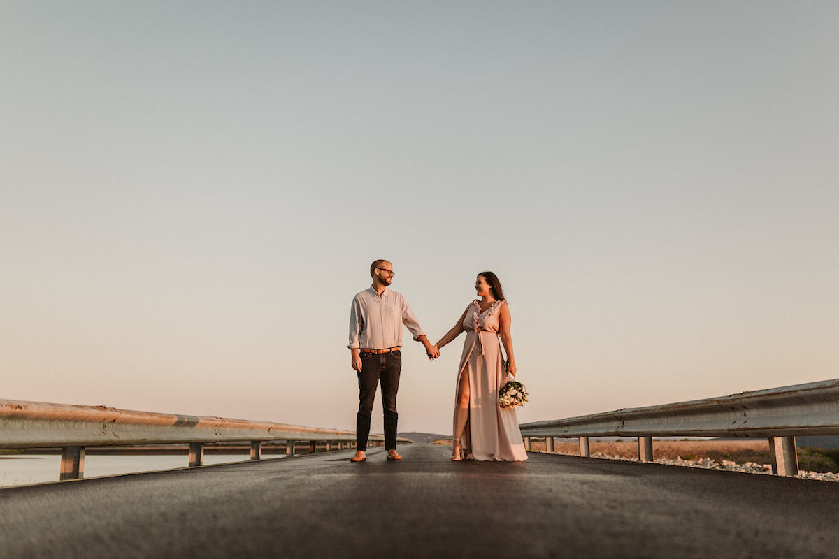 Man and woman stands hand-in-hand on Raccoon Mountain's loop drive at golden hour. She holds a bouquet of white flowers.