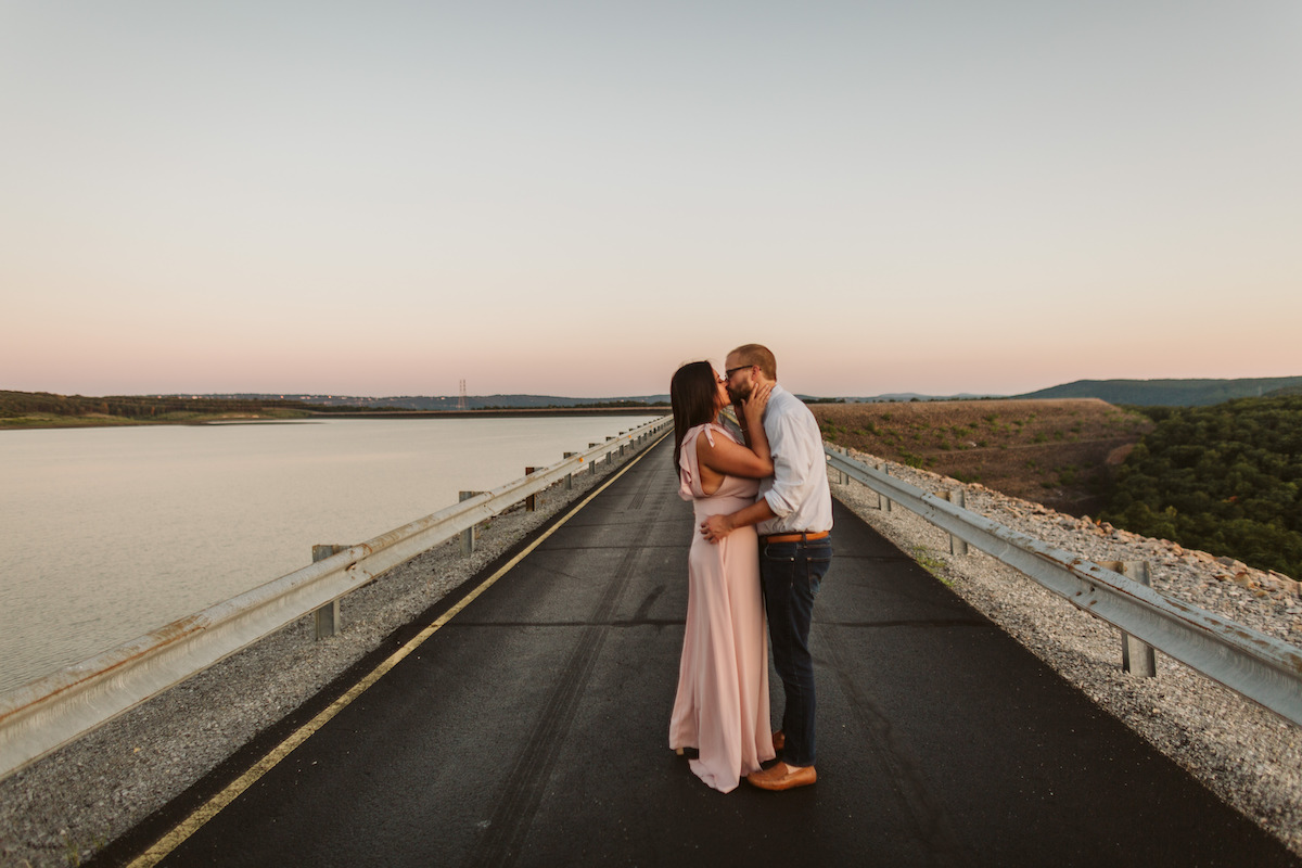 Man and woman stand kissing on Raccoon Mountain's loop drive at golden hour.