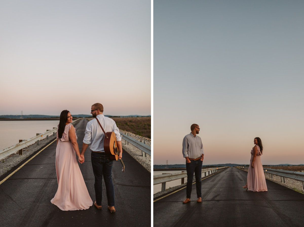 Man and woman walk hand-in-hand on Raccoon Mountain's loop drive at golden hour. He has a guitar hung over his shoulder.