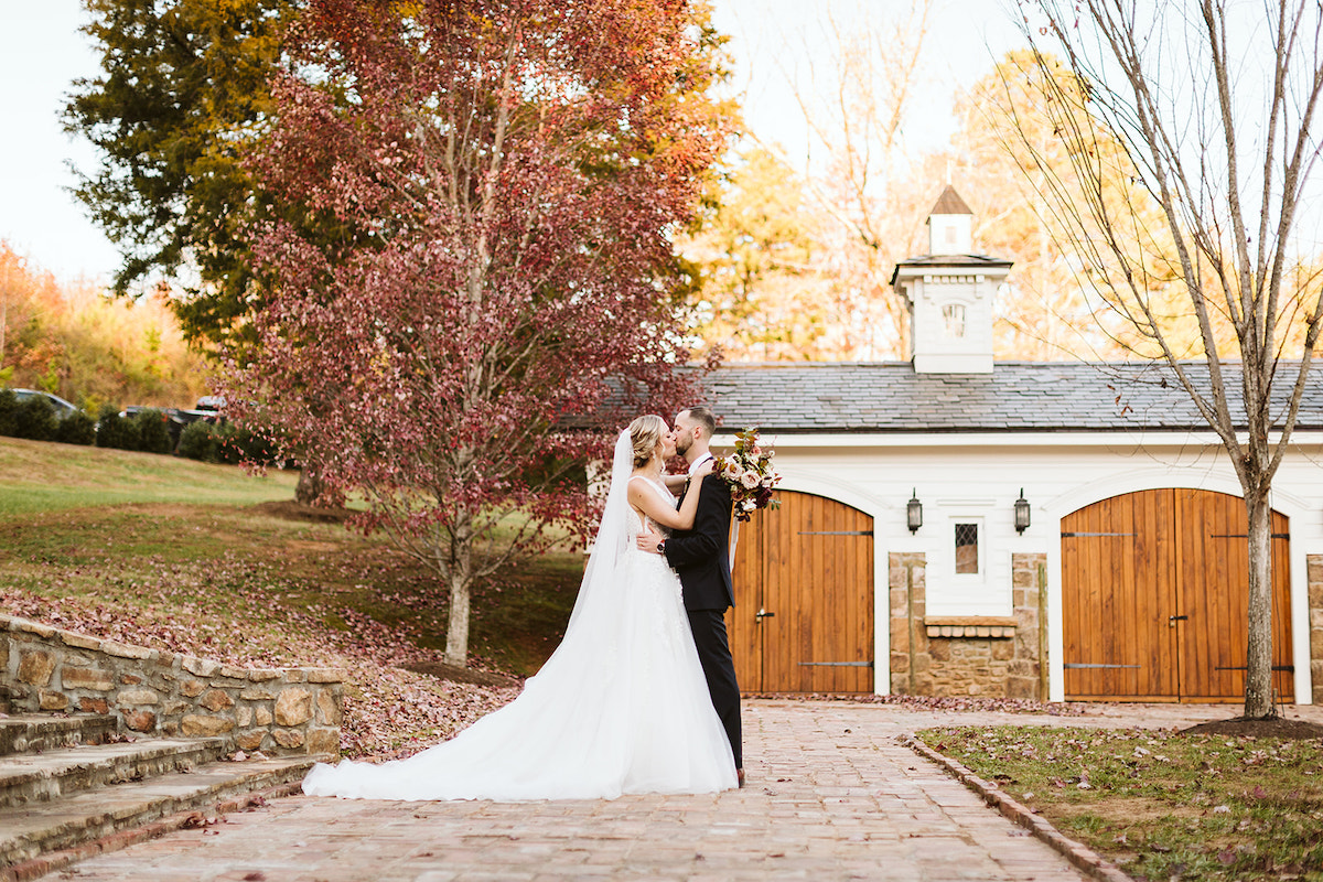 Bride and groom kiss on antique brick carriage path in front of carriage house at The Homestead at Cloudland Station