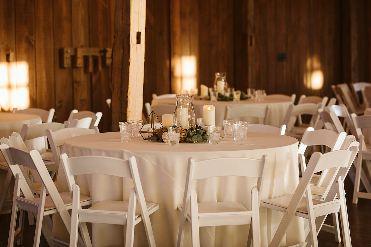 White Table linens and simple table decorations on round table surrounded by white wooden folding chairs