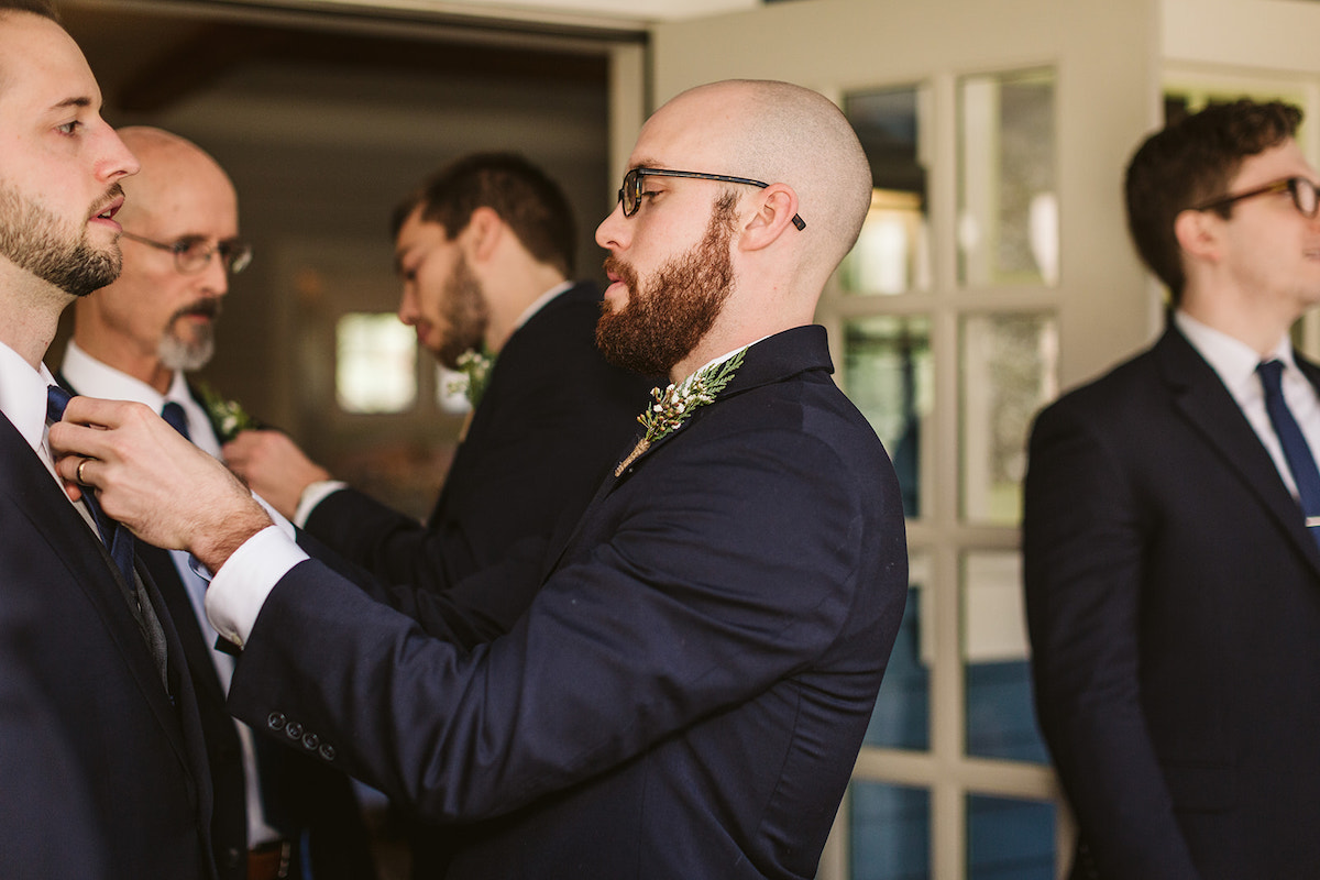 Groomsman in dark jacket and simple boutonniere straightens the groom's tie knot