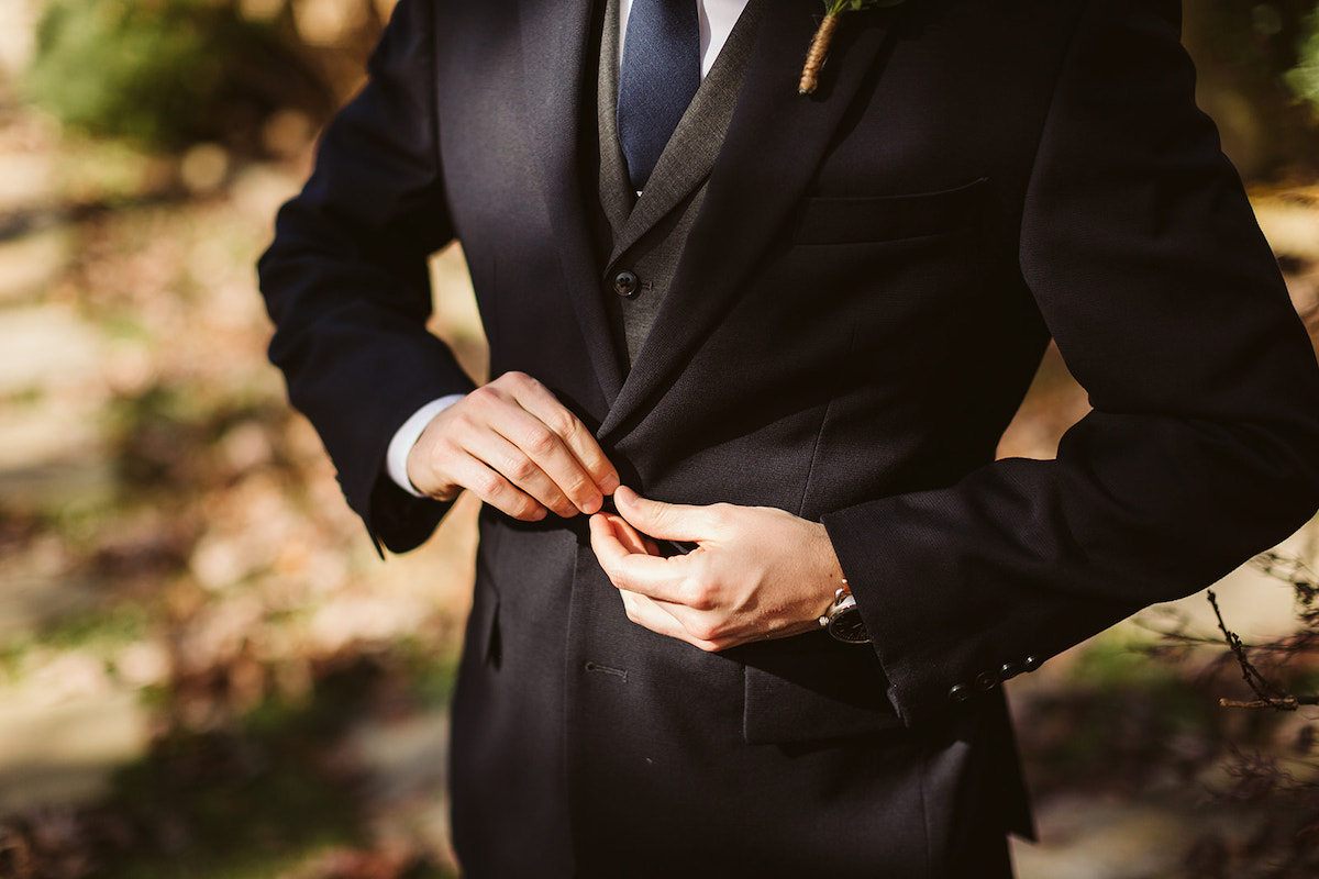 Man buttons the top button of his dark suit jacket