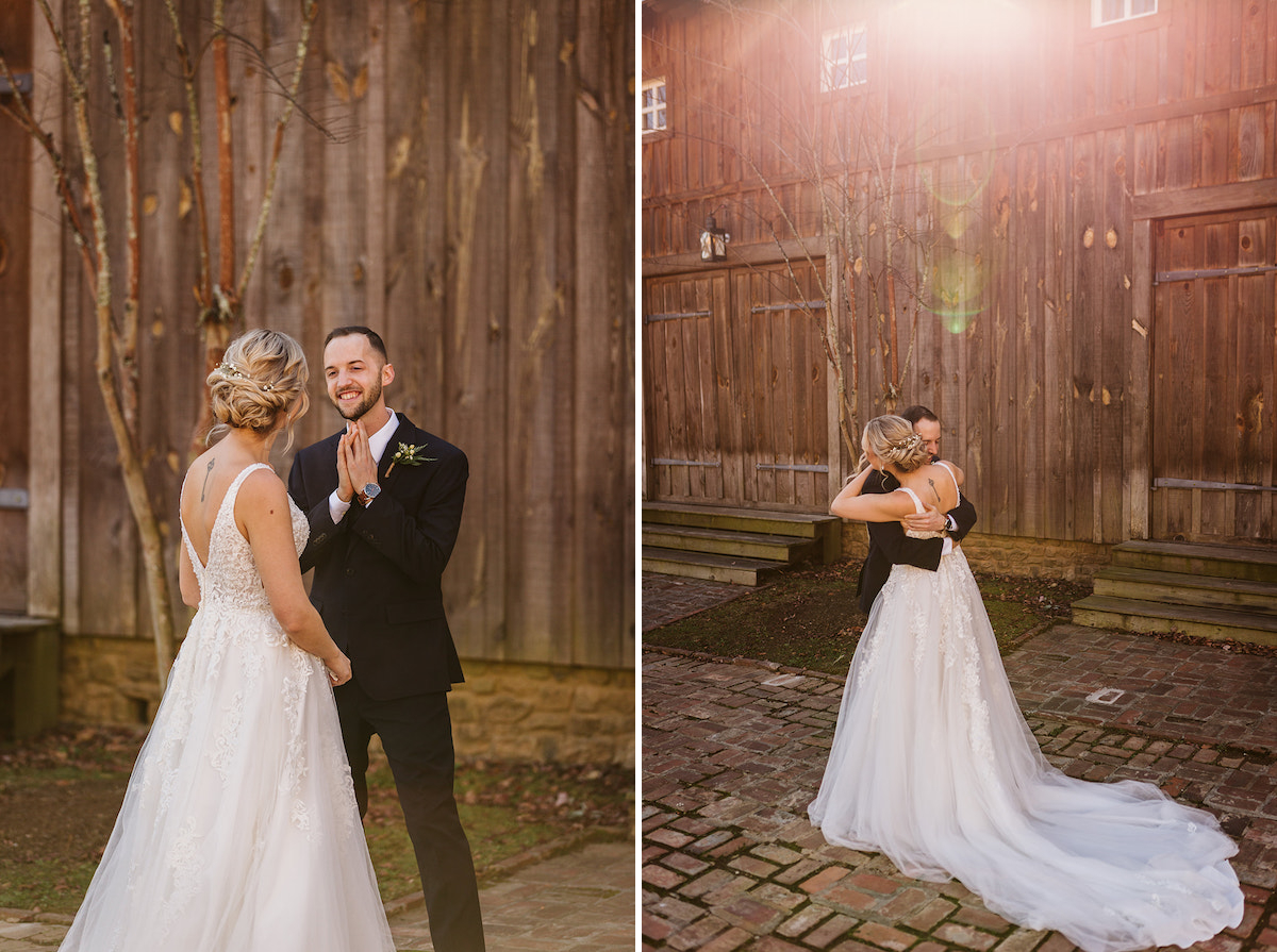 Bride and groom first look on brick path in front of tall wooden barn. Groom smiles, clasping his hands under his chin.