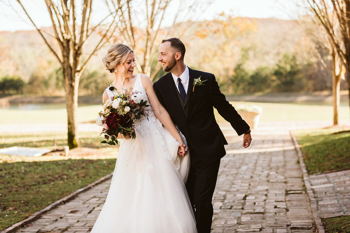 Bride and groom smile at each other as they walk down antique brick carriage path