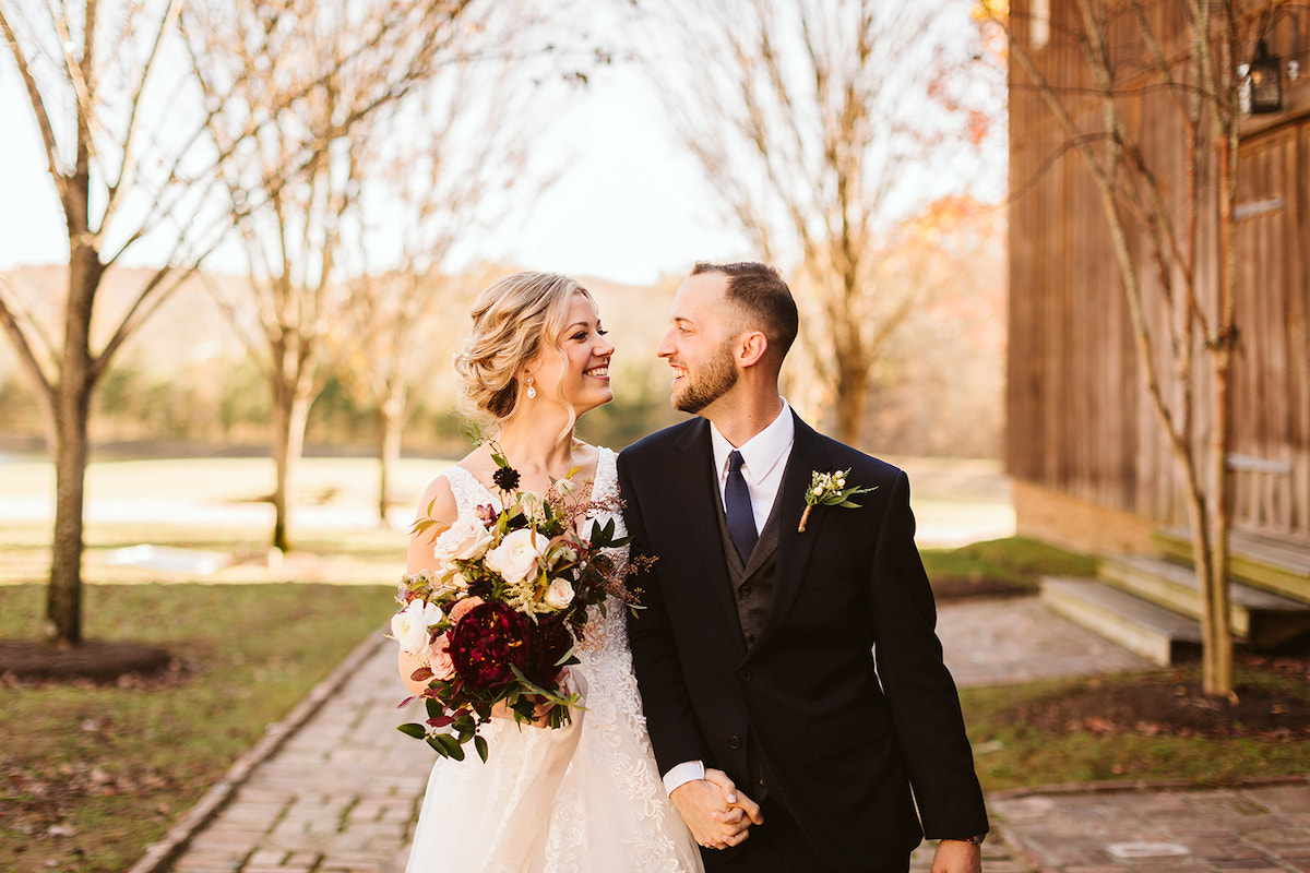 Bride and groom smile at each other as they walk down antique brick carriage path