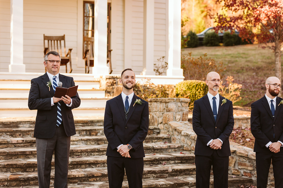 Groom, officiant, and groomsmen stand in front of wide stone stairs