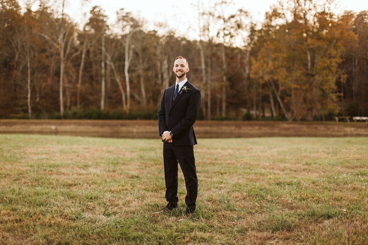 Man in dark suit stands in a grassy field.