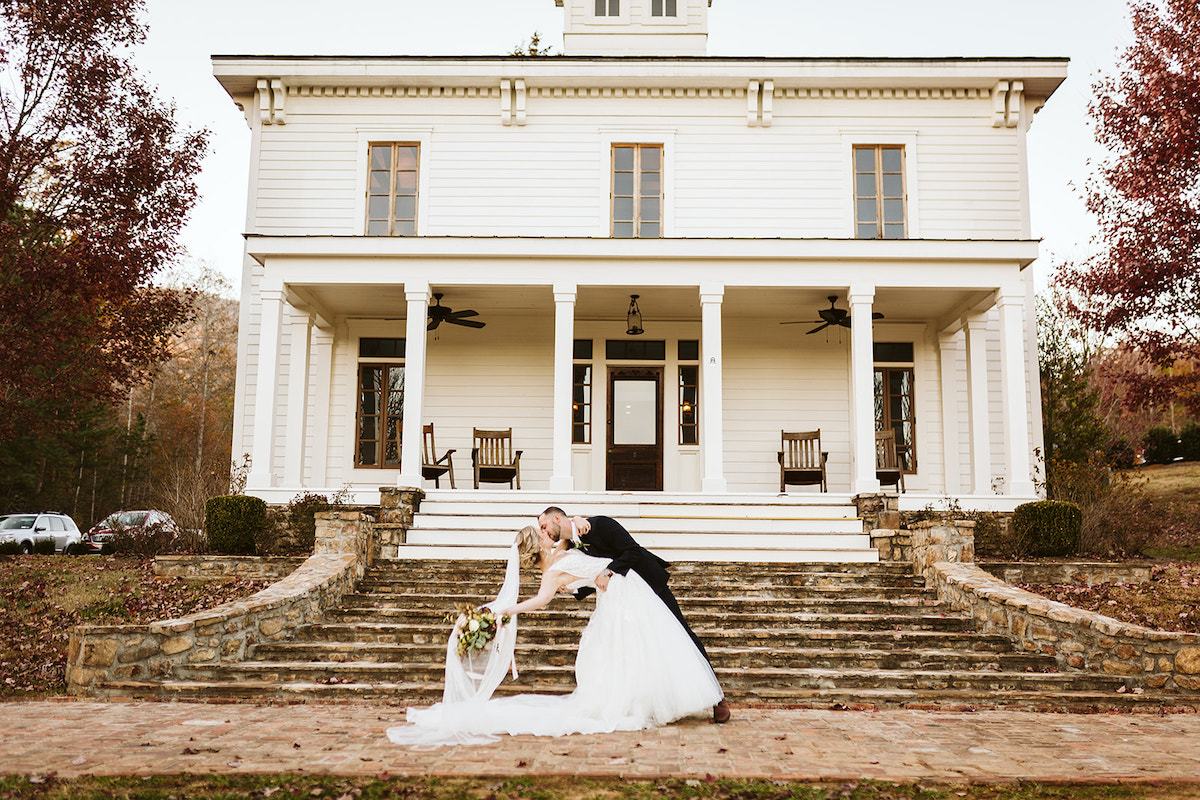 Groom dips bride low for a kiss. She holds her bouquet behind her as her veil streams to the ground.