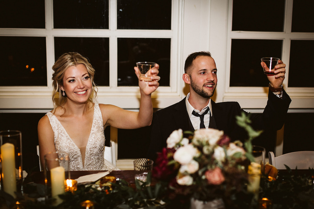 Bride and groom sit and raise glasses as they are toasted