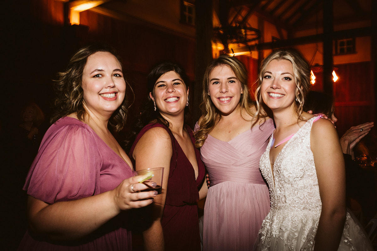 Bride stands with several bridesmaids who wear shades of pink and maroon dresses