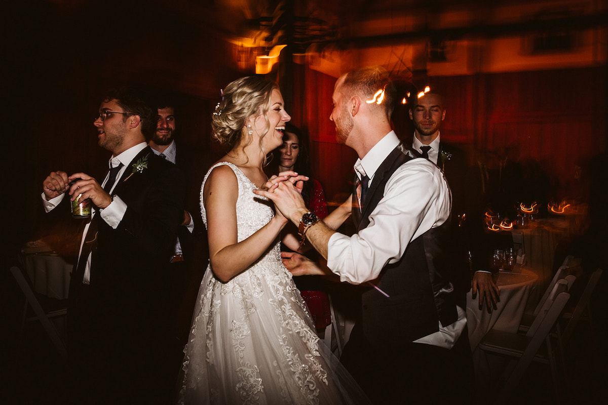 Bride and groom laugh with each other as they dance surrounded by wedding guests