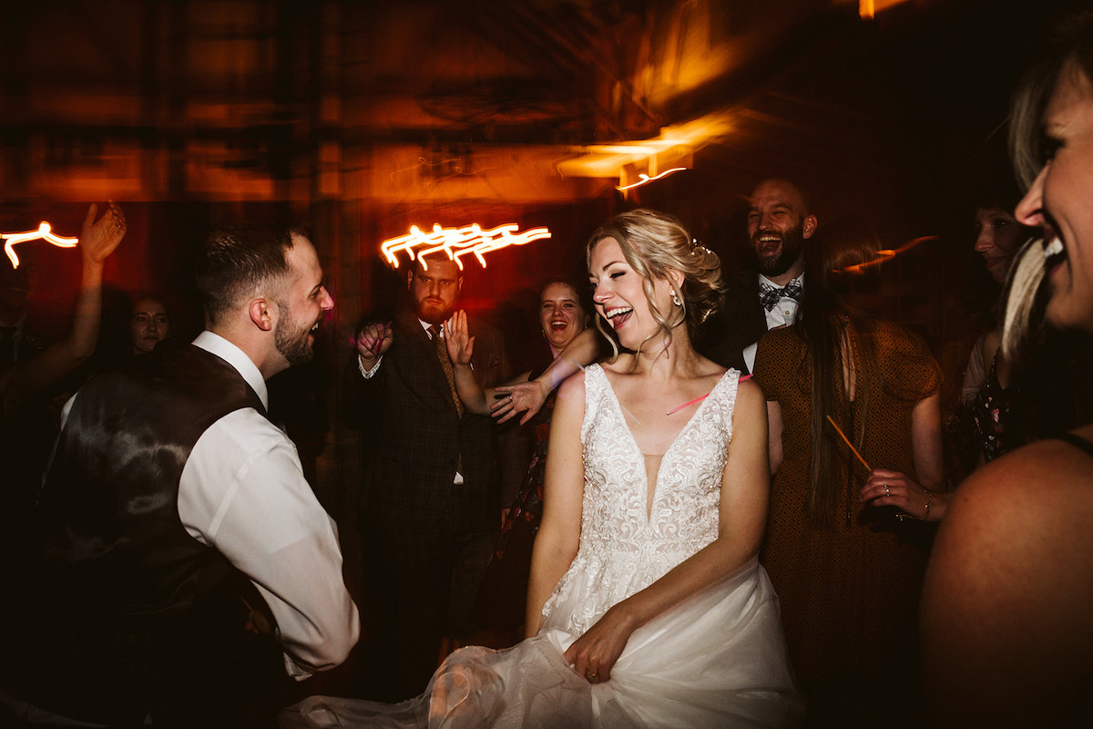 Bride and groom laugh with each other as they dance surrounded by wedding guests