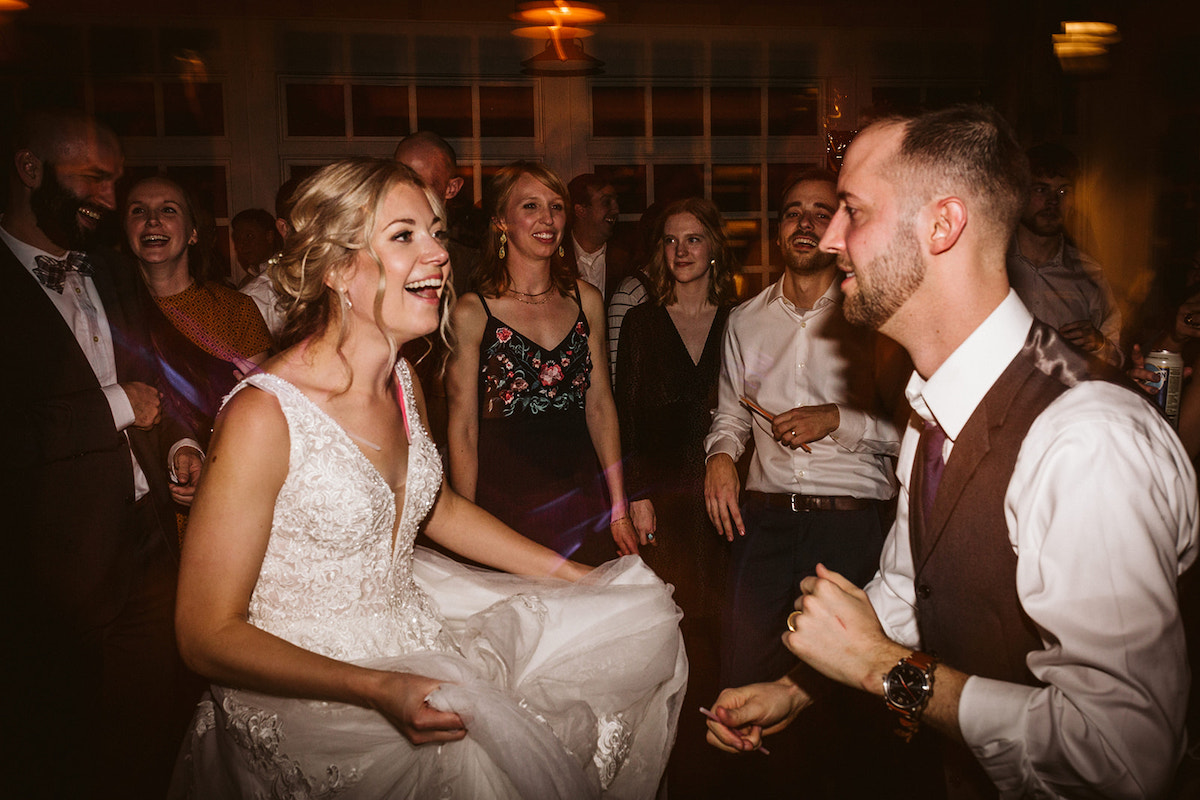 Bride holds up her dress as she and her groom dance surrounded by friends