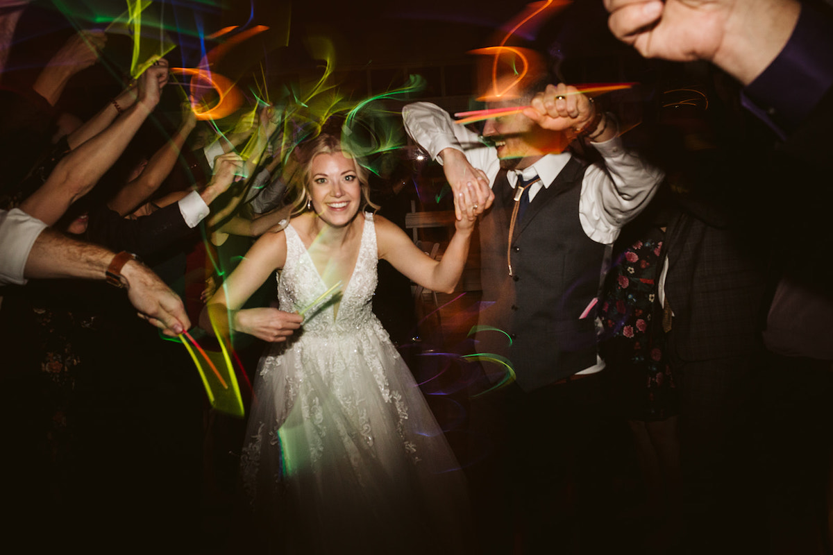 Bride and groom hold hands and duck between waving glow sticks