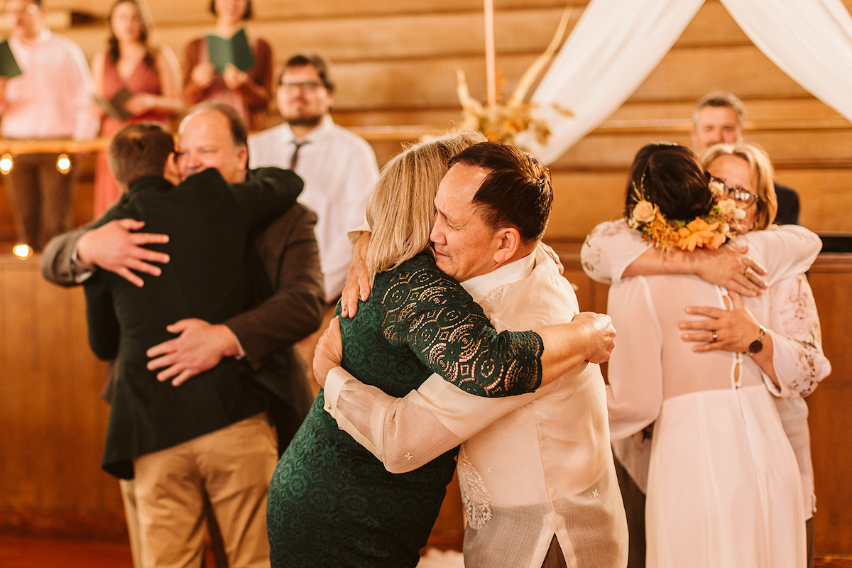 Man in white shirt hugs woman in green dress while others hug behind them