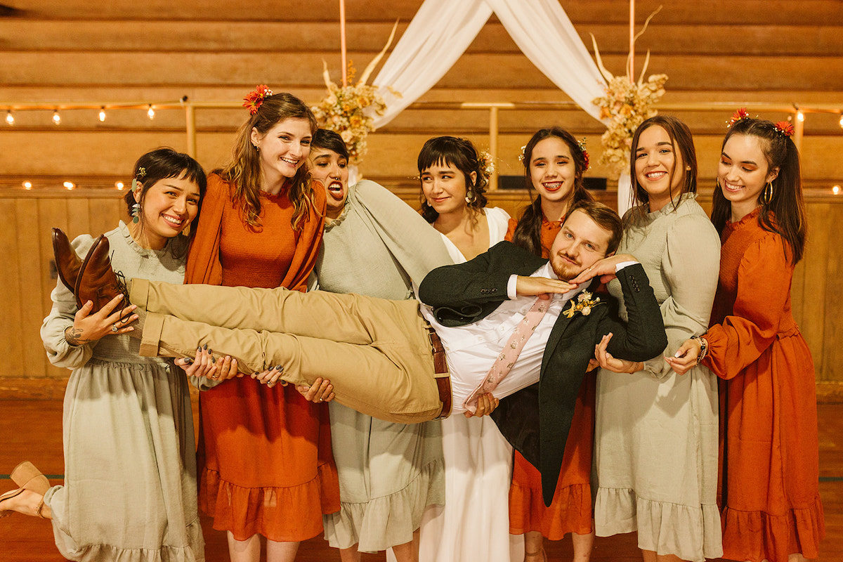 Bride and bridesmaids elevate groom who poses with his hands under his chin