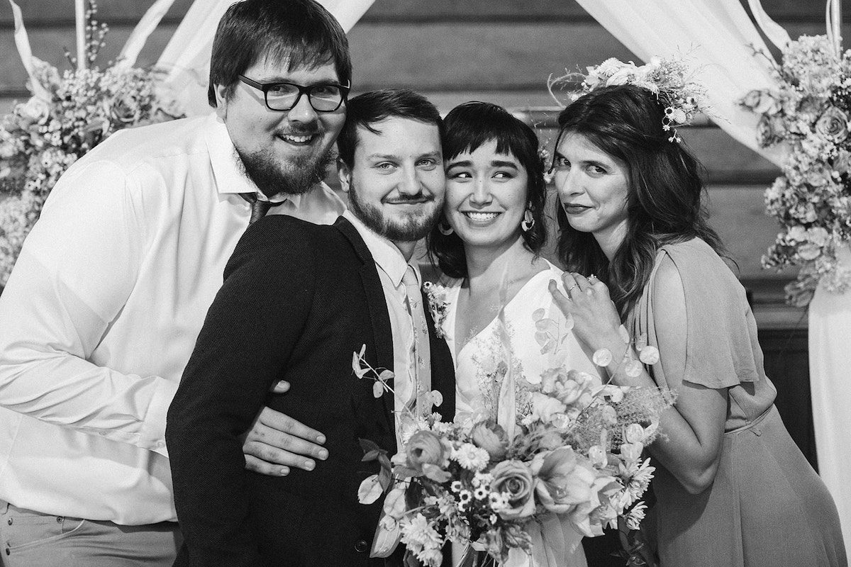 Bride and groom and their best man and maid of honor make silly faces under their wedding arch