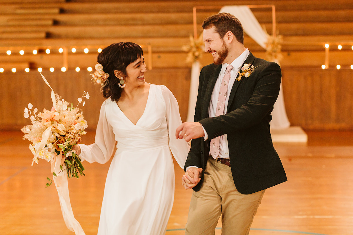 Bride and groom look at each other as they walk through a school gym